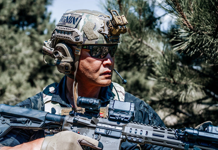 Soldier in tactical helmet and headset wearing Green Beret Foundation x GATORZ Sentix sunglasses outdoors among pine trees